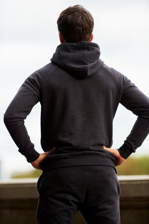 A back view of man posing for camera while wearing a black marl fitness hoodie