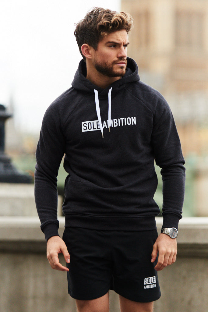 Athlete wearing a men's black marl muscle fit hoodie on way to gym, with london parliament buildings in background