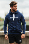 Young man wearing a men's navy marl slim fit pullover hoodie with zip pockets and white logo print.