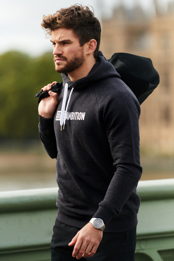 Side shot of man walking with bag over shoulder wearing a black slim fit men's hoodie with zip pockets and logo 