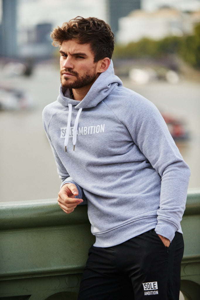 Young man leans on ledge while sporting a trendy slim fit gym training hoodie with zips and pockets
