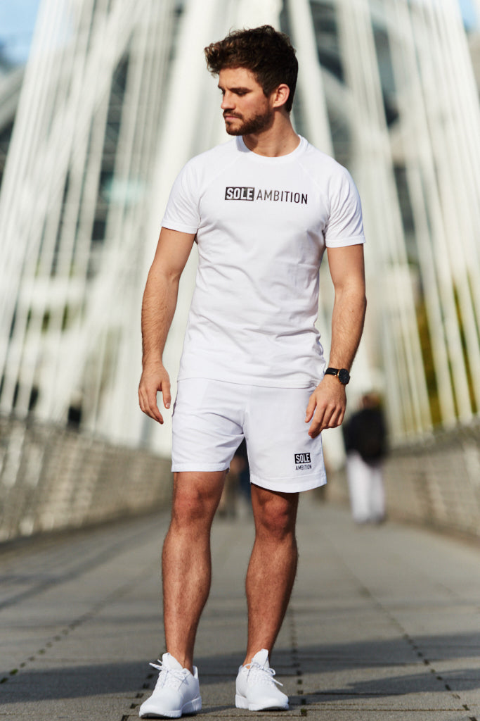 Man posing on a London bridge with a Sole Ambition white cotton training top and polyester shorts on