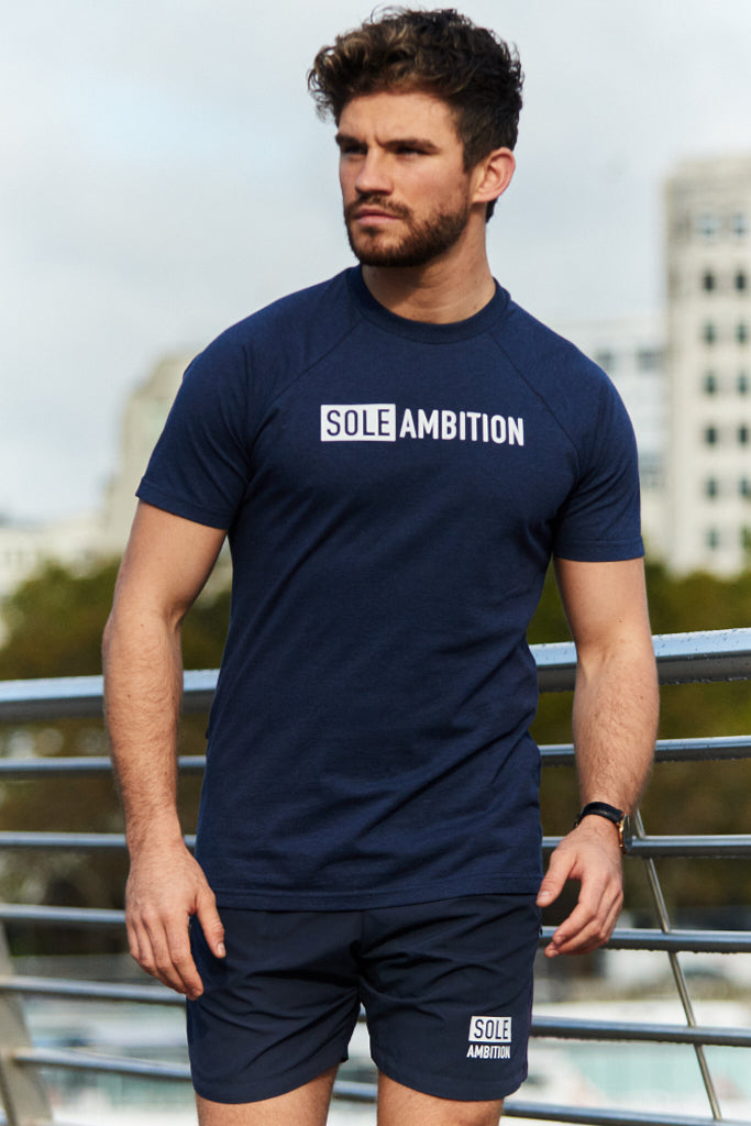 Man poses while wearing a navy sports fit gym t-shirt with London buildings in the background
