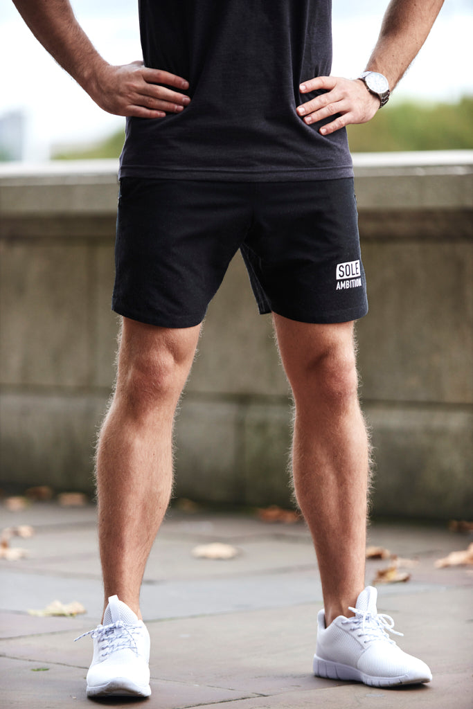 Man on street wearing slim fit black Sole Ambition workout shorts with white print and zip pockets