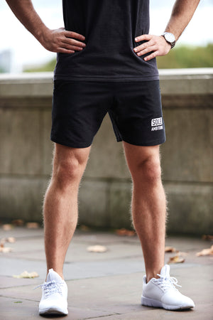 Man on street wearing slim fit black Sole Ambition workout shorts with white print and zip pockets